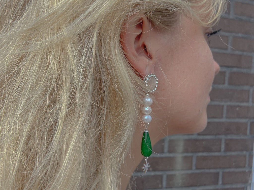 Mae geboortesteen oorbellen met een unieke natuurlijke zoetwaterparel en fonkelend helder Swarovski kristal, modern strak design van Néhlia in vrouwen oor gedragen.