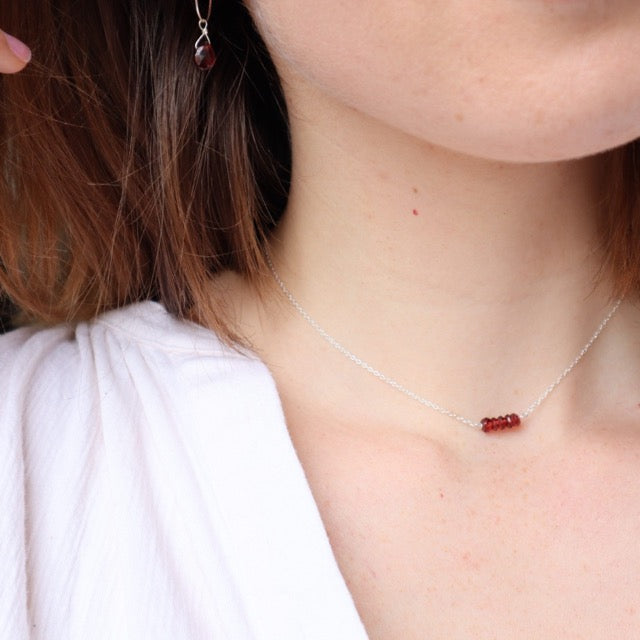 De Orb geboorteketting met granaat gedragen voor een strakke en elegante uitstraling.